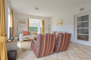 Un salon comprenant un canapé, deux fauteuils à rayures, un téléviseur et une fenêtre avec des rideaux.