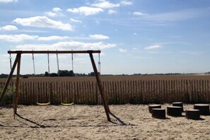 Eine Schaukel im Sand mit einem Feld im Hintergrund.