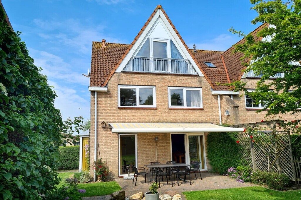Ein zweistöckiges Haus mit einer Terrasse, einem überdachten Sitzbereich und einem Garten.