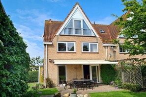 Ein zweistöckiges Haus mit einer Terrasse, einem überdachten Sitzbereich und einem Garten.
