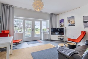 A modern living room with a sofa, a TV, a desk, and a chair. - Domburgseweg 52 Apartment (Oostkapelle)