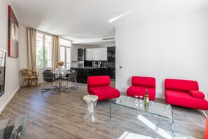 Un salon moderne avec une table basse en verre, des canapés rouges et un coin repas comprenant une table et des chaises en verre.