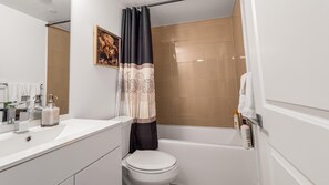 Une salle de bain équipée de toilettes, d’une baignoire, d’un rideau de douche et d’un lavabo avec des articles de toilette.