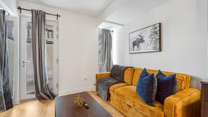 A living room with a yellow sofa, grey and blue cushions, a wooden coffee table, and a framed picture on the wall. - StayToronto - Modern 1BR and Den - Sleeps 6 in Downtown Toronto (Toronto)