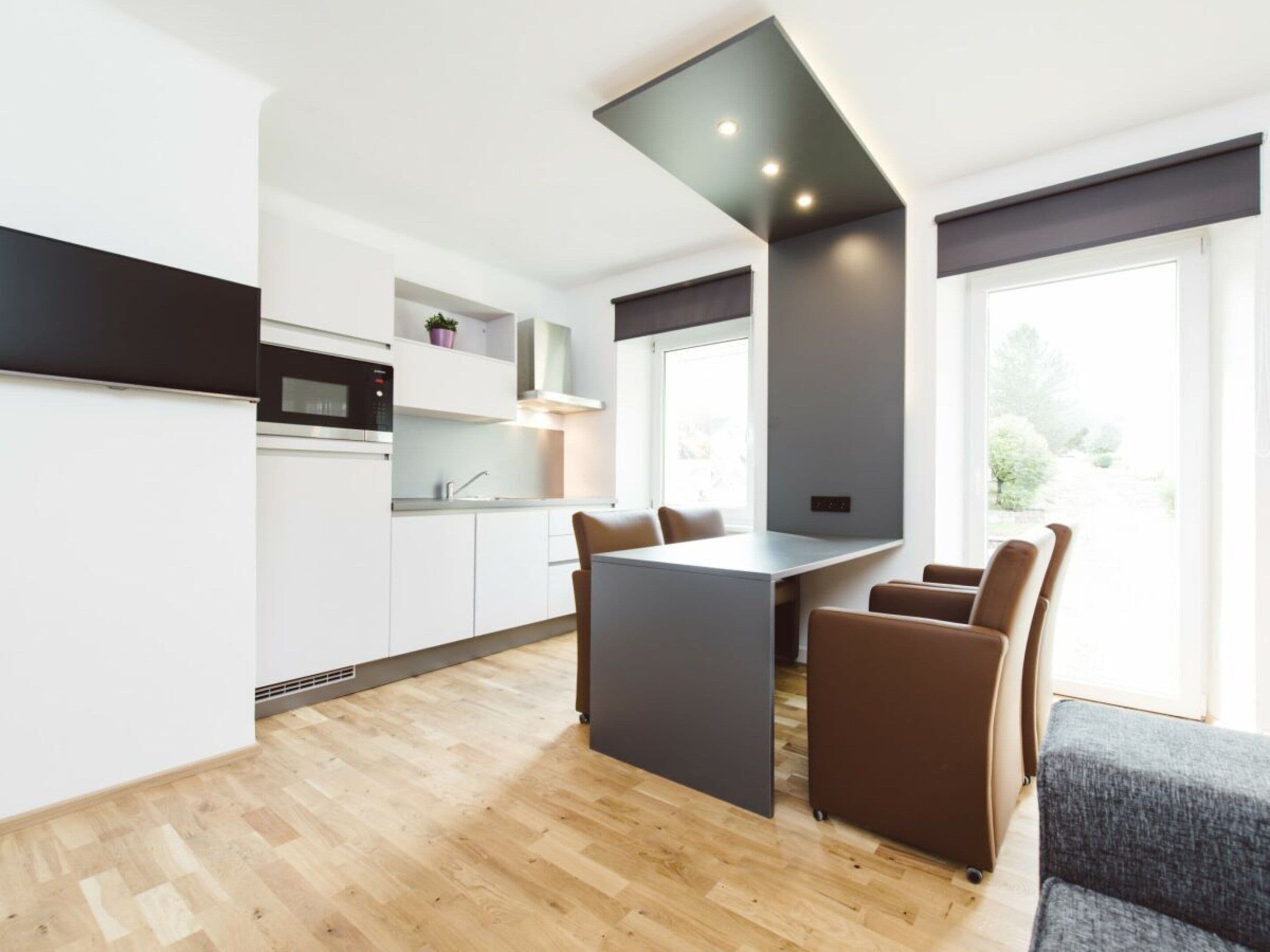 A modern kitchen with a central island, dining chairs, and a view of the outdoors.