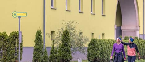 A yellow building with a clear sky, a sidewalk, and a dog walking with two people.
