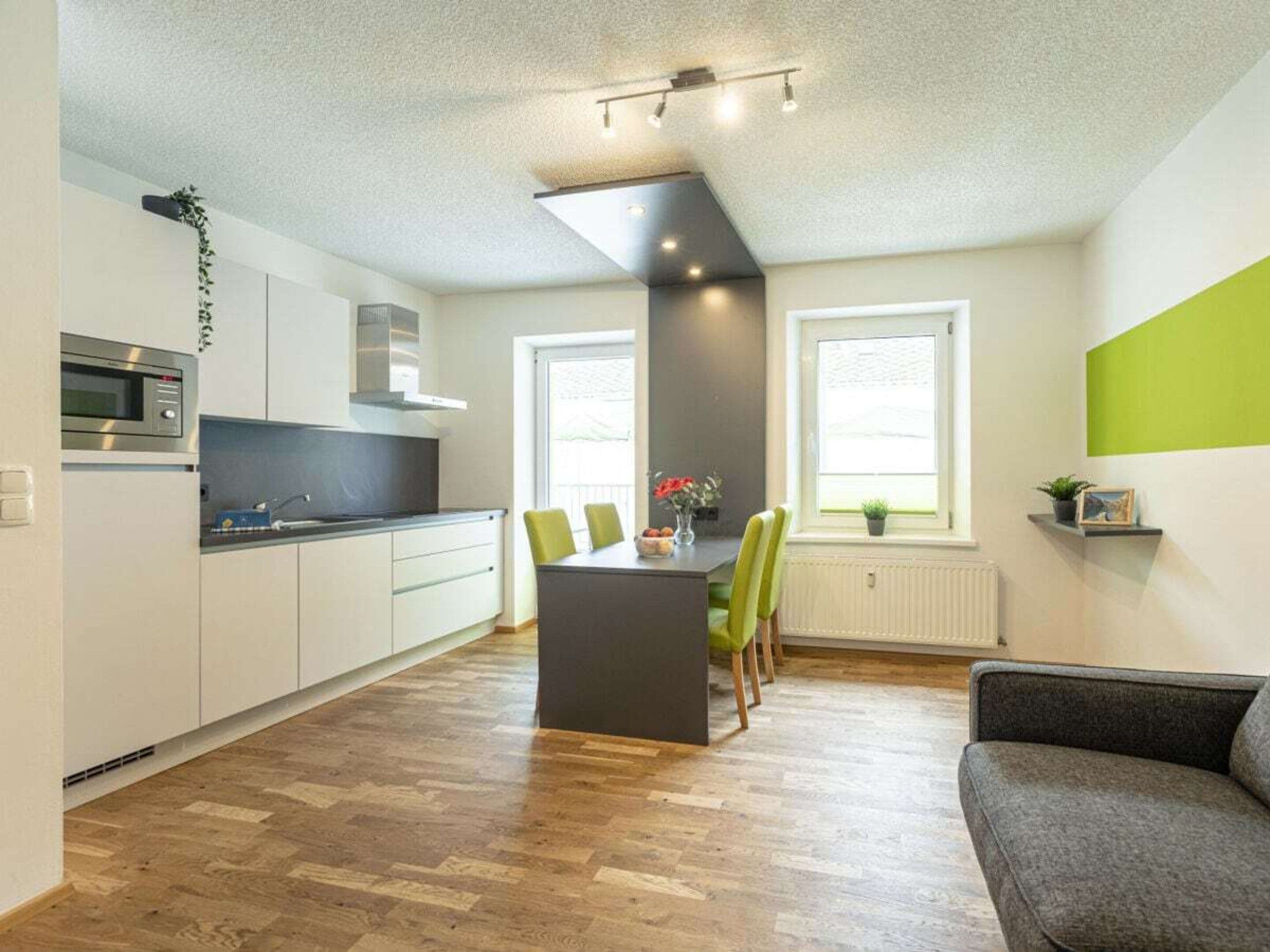 A modern kitchen with white cabinets, a built-in oven, and a dining area with a central island and chairs.