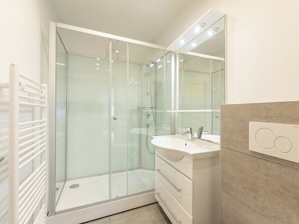 A modern bathroom with a glass-enclosed shower, a white vanity with a mirror, and a beige tiled wall. - Classic Holiday Apartment I (Eisenerz)