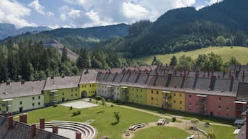 A courtyard with a swimming pool, surrounded by multi-story buildings with a sloped roof, set against a backdrop of mountains and a clear sky.