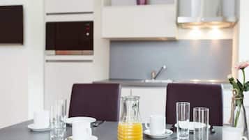 A dining table set with plates, glasses, and a bottle of orange juice in a modern kitchen with a microwave and cabinets.