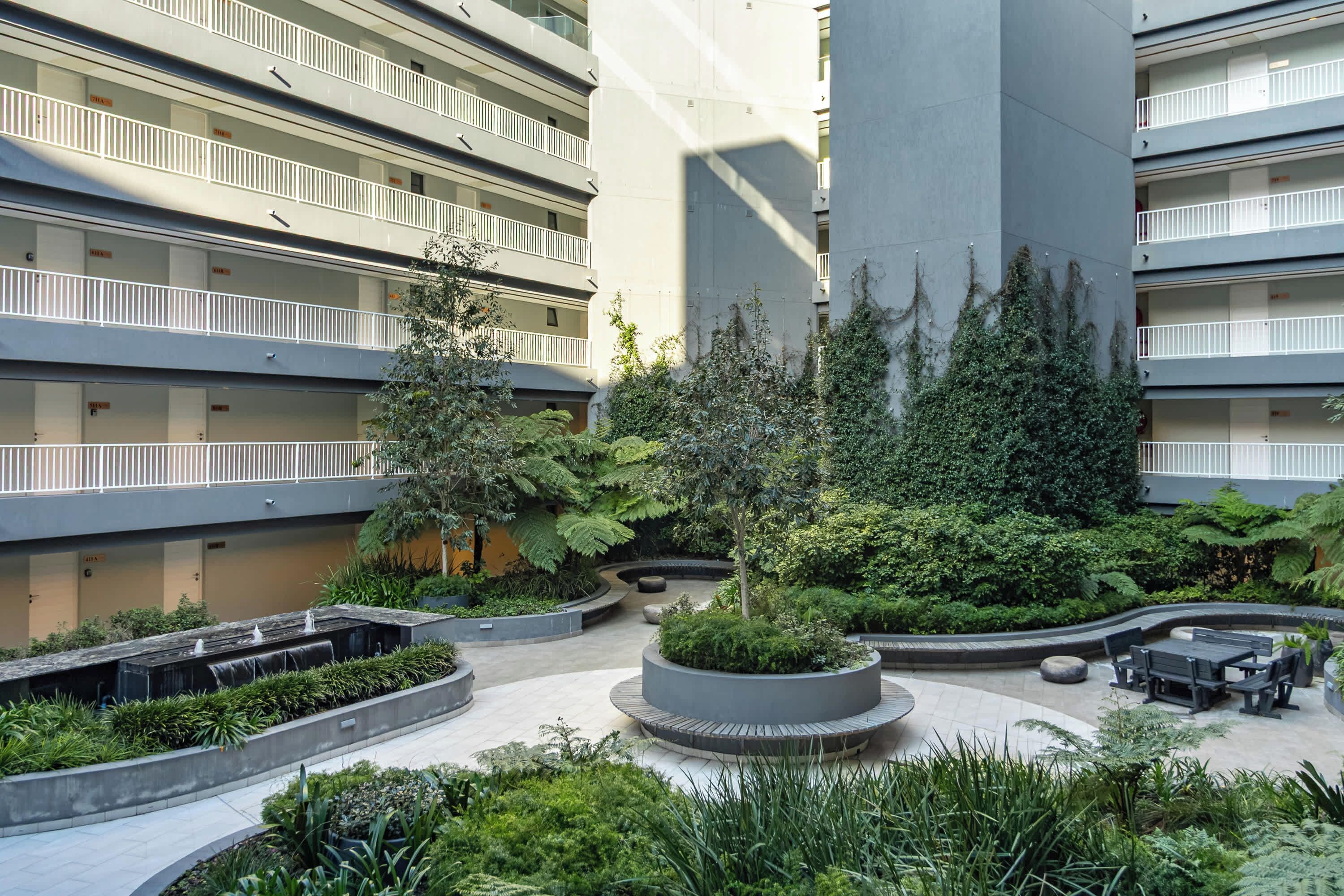 A multi-story building with balconies, a central courtyard with greenery, and outdoor seating.