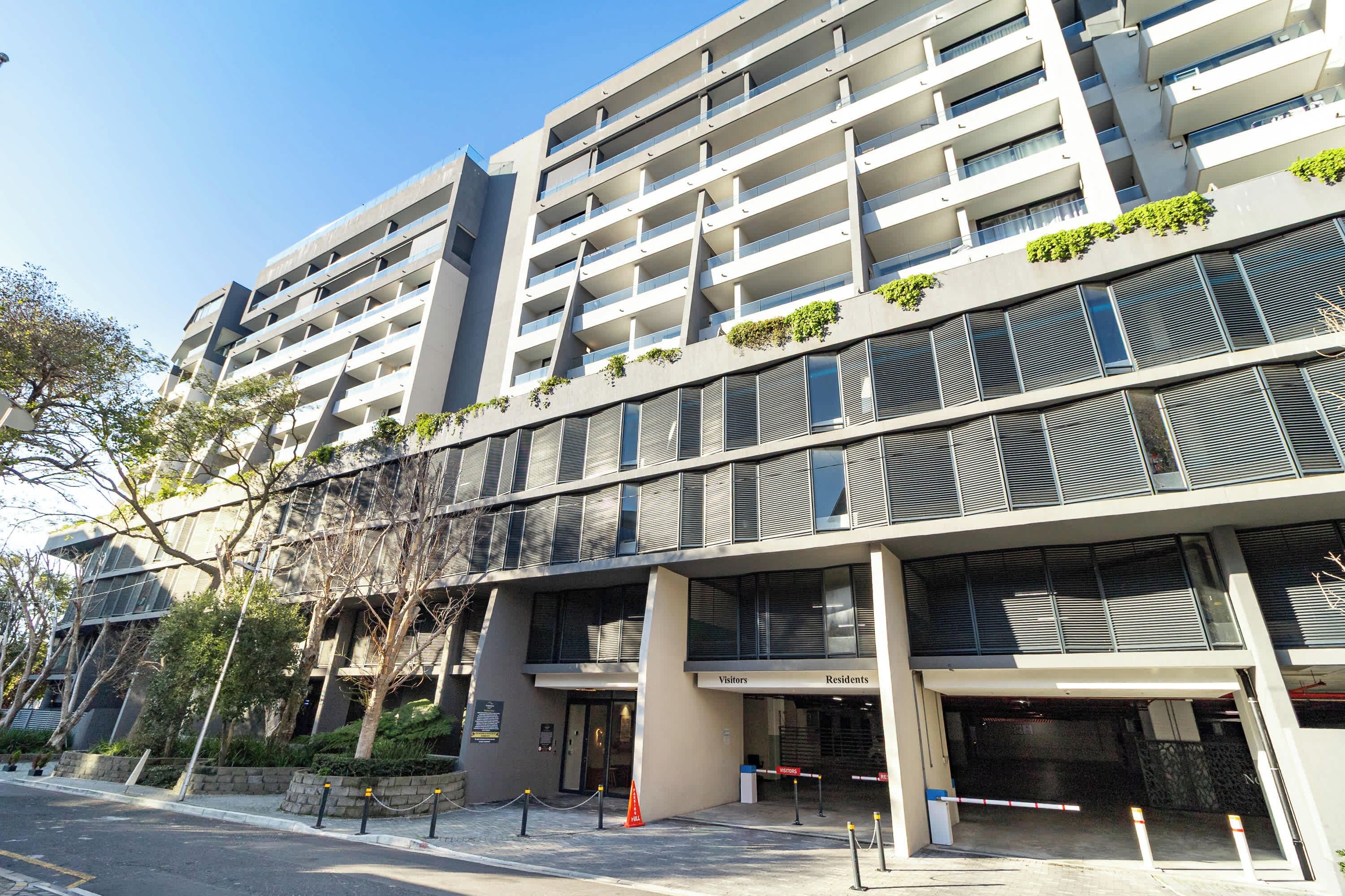 A multi-story hotel with a modern architectural design, featuring balconies and a gated entrance.