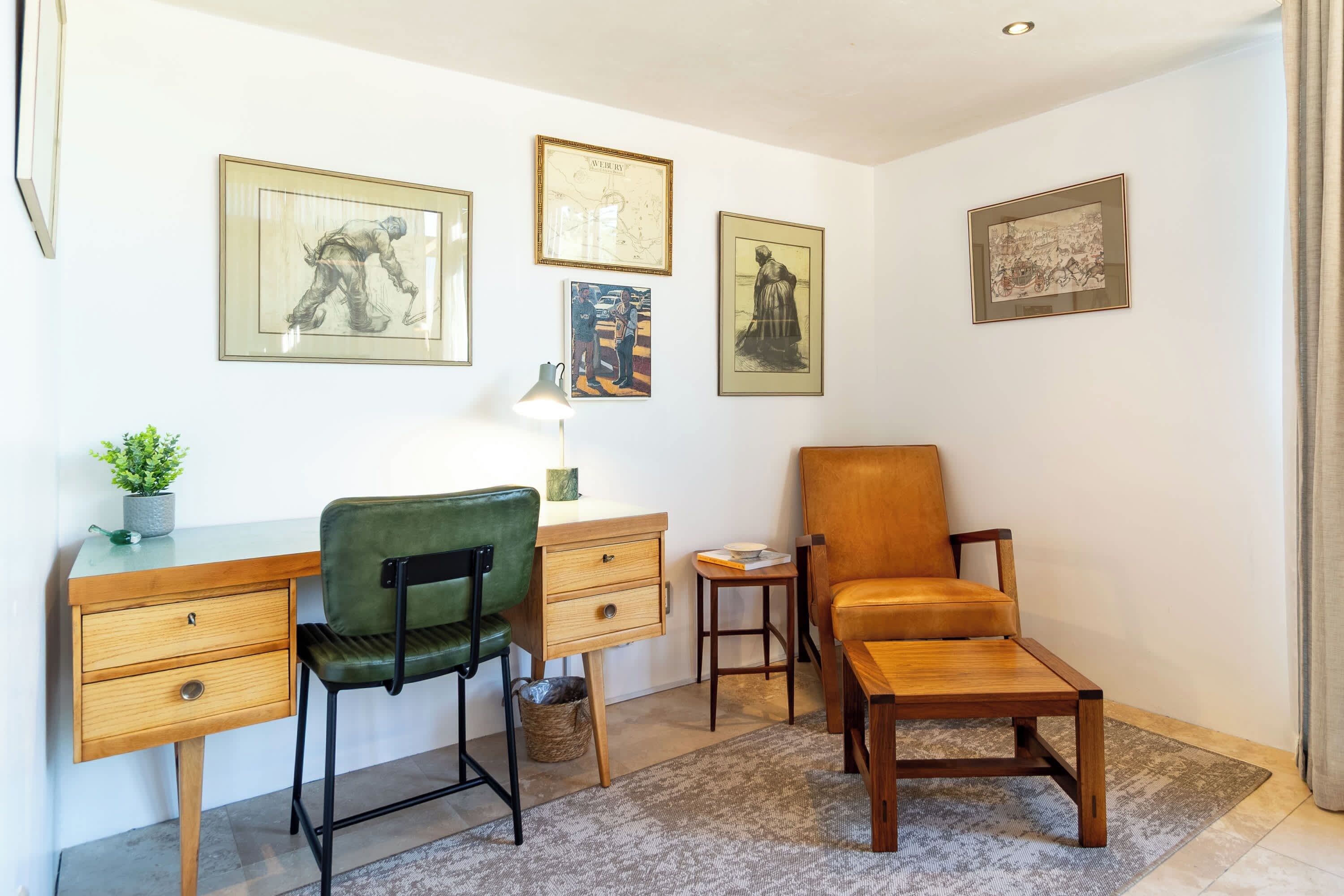 Une pièce comprenant un bureau, deux chaises, une petite table et un tapis. Des tableaux encadrés ornent le mur.