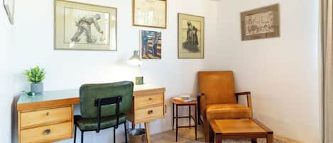 A room with a desk, two chairs, a small table, and a rug. There are framed pictures on the wall.