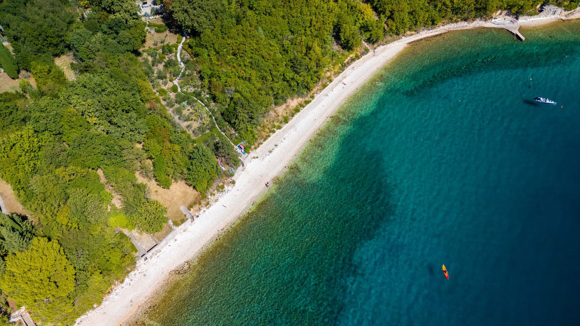 An aerial view of a coastal area with a beach, clear water, and dense greenery.