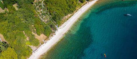 An aerial view of a coastal area with a beach, clear water, and dense greenery.