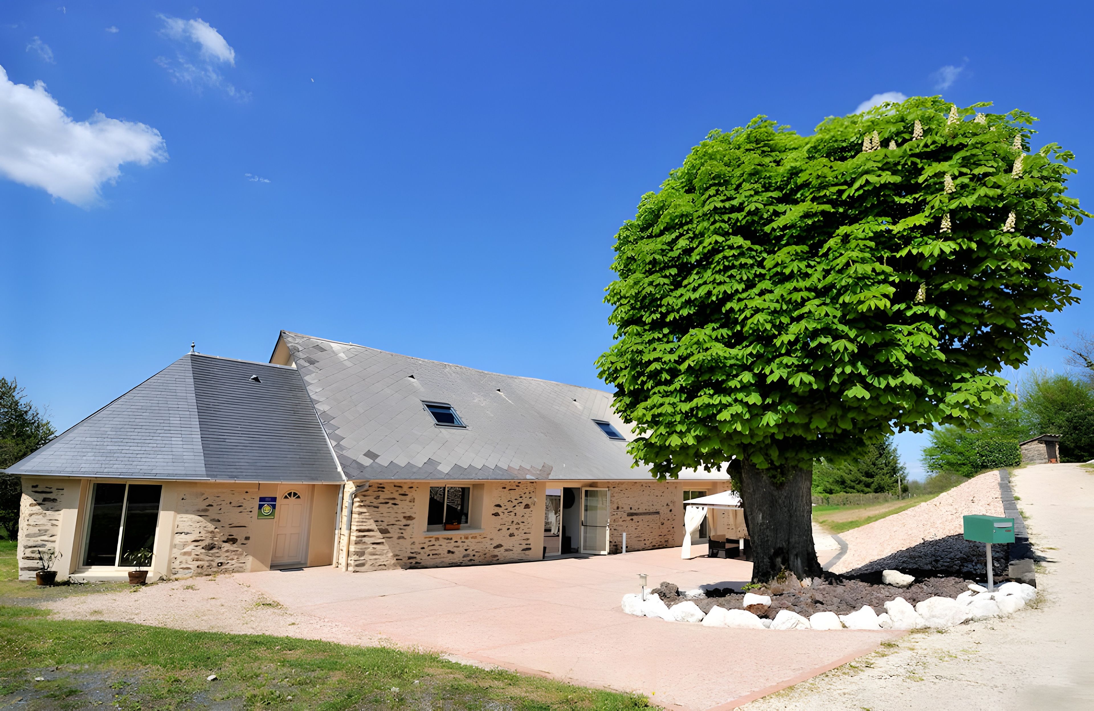A stone building with a sloped roof and a large tree in front.