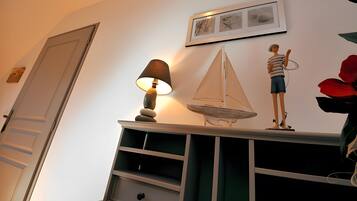 Une pièce avec une porte, une étagère fixée au mur sur laquelle se trouve une lampe, une petite maquette de voilier et un tableau encadré.