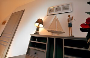 Ein Zimmer mit einer Tür, einem an der Wand befestigten Regal mit einer Lampe, einem kleinen Segelbootmodell und einem gerahmten Bild.