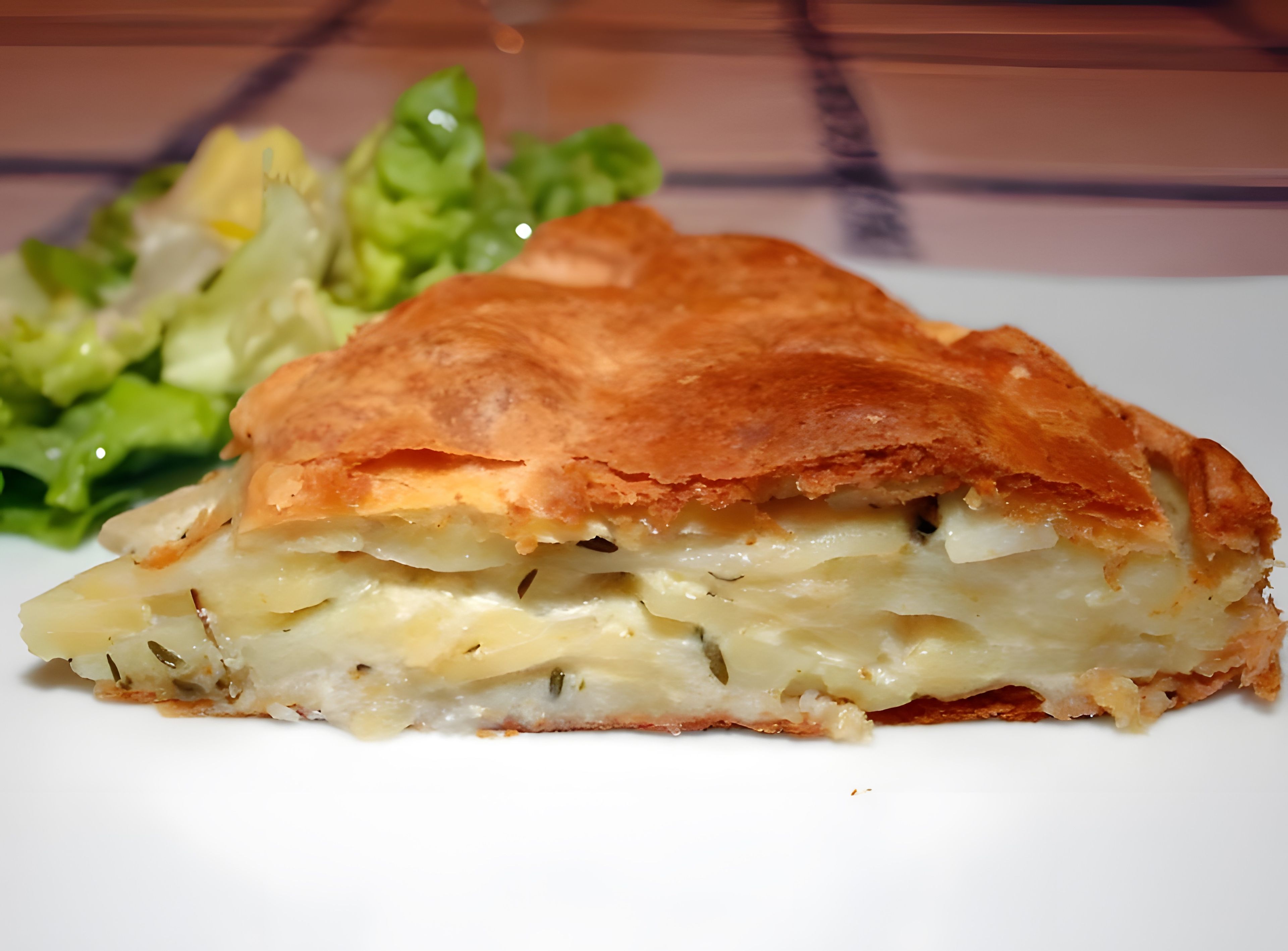 A slice of layered pastry with cheese and herbs, accompanied by a side salad.