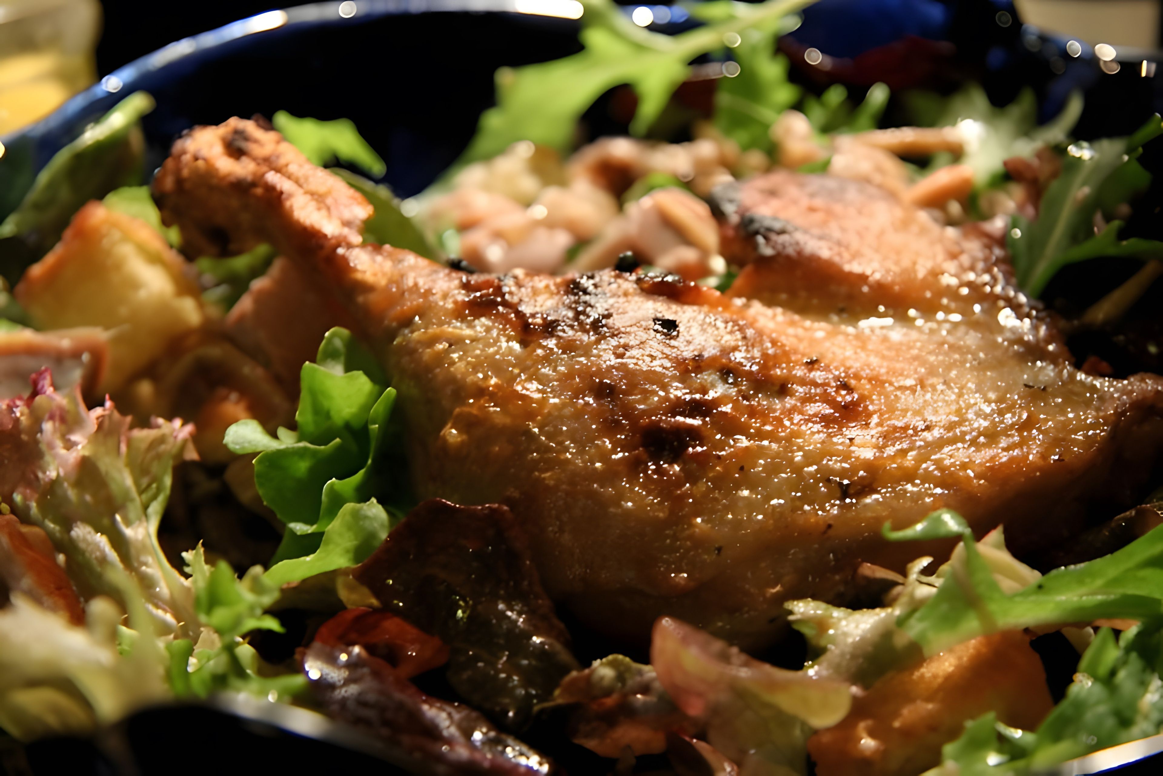 A close-up of a cooked chicken leg with crispy skin, served on a bed of mixed greens and vegetables.