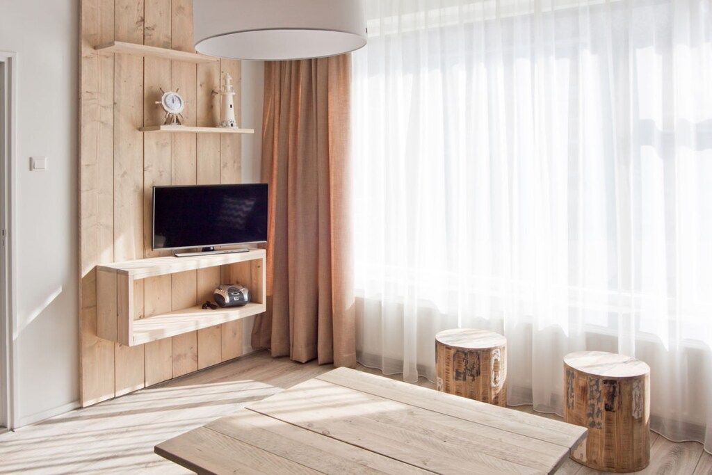 A living room with a wooden TV stand, a flat-screen TV, and two wooden stools.
