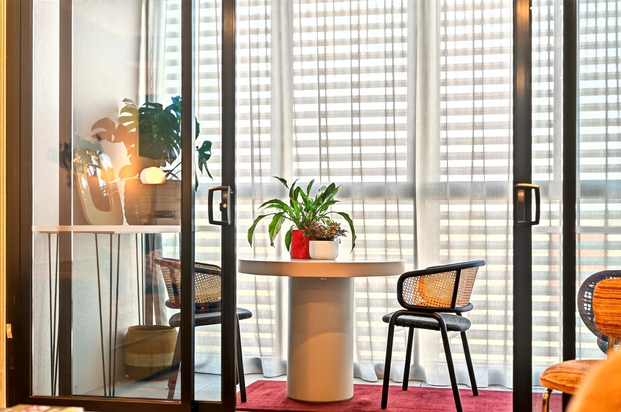 A room with a round table, two chairs, a potted plant, and a window with blinds.
