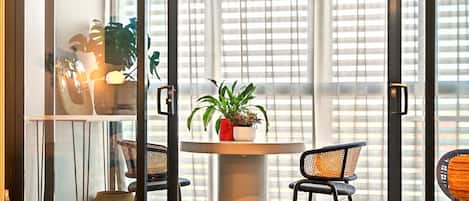 Ein Zimmer mit einem runden Tisch, zwei Stühlen, einer Topfpflanze und einem Fenster mit Jalousien.