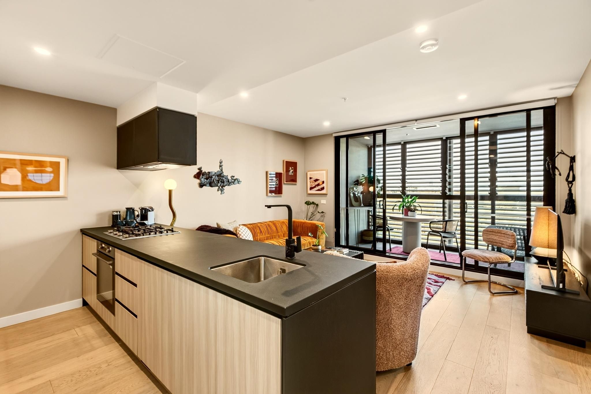 A modern kitchen with a central island, a dining area with a sofa and chairs, and a large window with blinds.