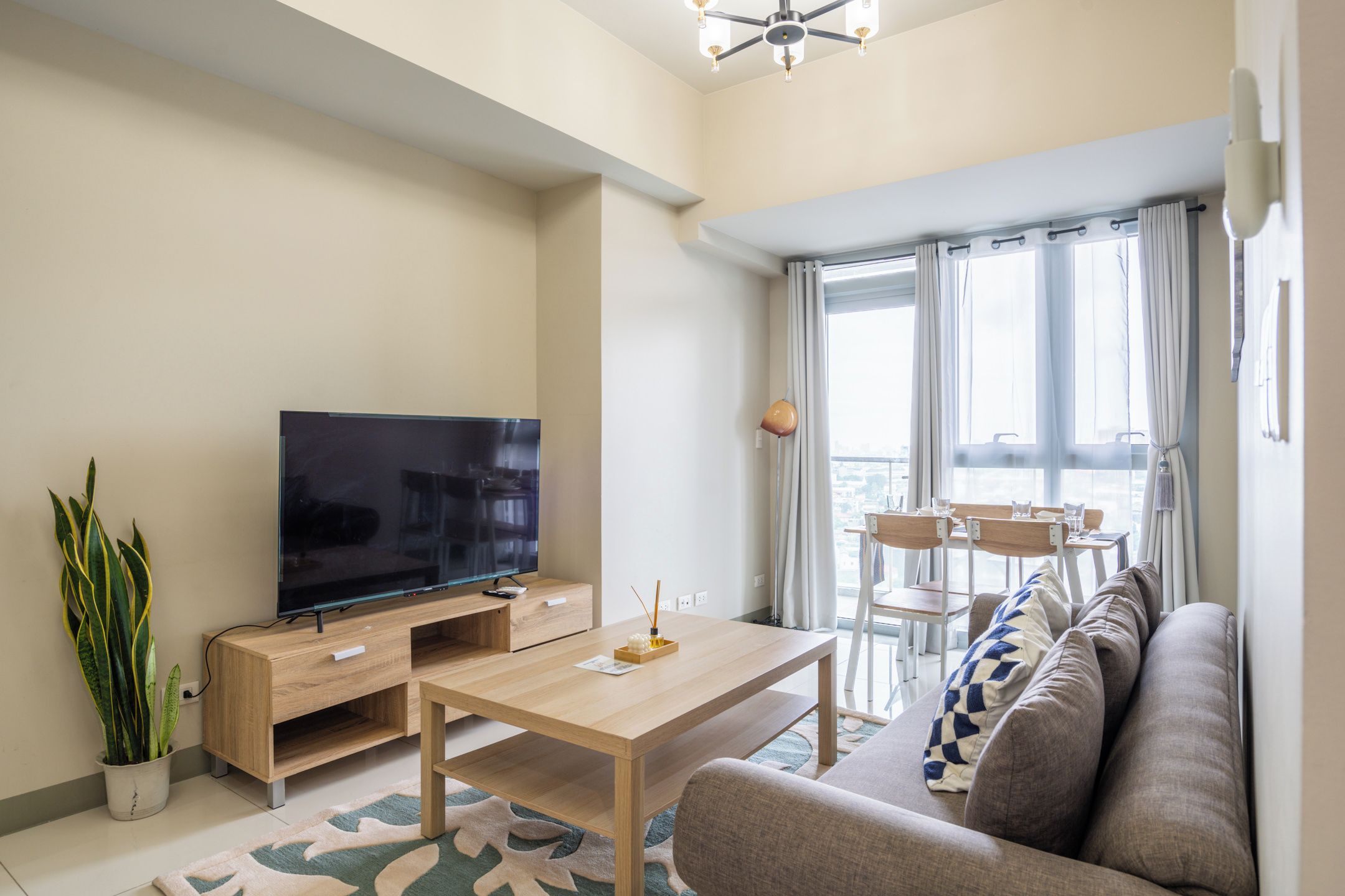 A modern living room with a flat-screen TV, wooden furniture, a sofa, and a dining area with chairs.