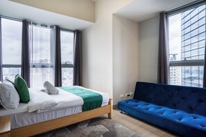 Ein modernes Schlafzimmer mit einem Bett, einem blauen Sofa und großen Fenstern mit Blick auf die Stadt.