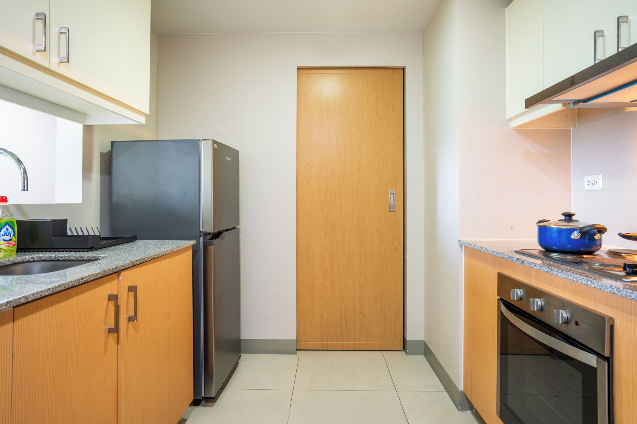A compact kitchen with a refrigerator, oven, and a blue pot on the countertop.
