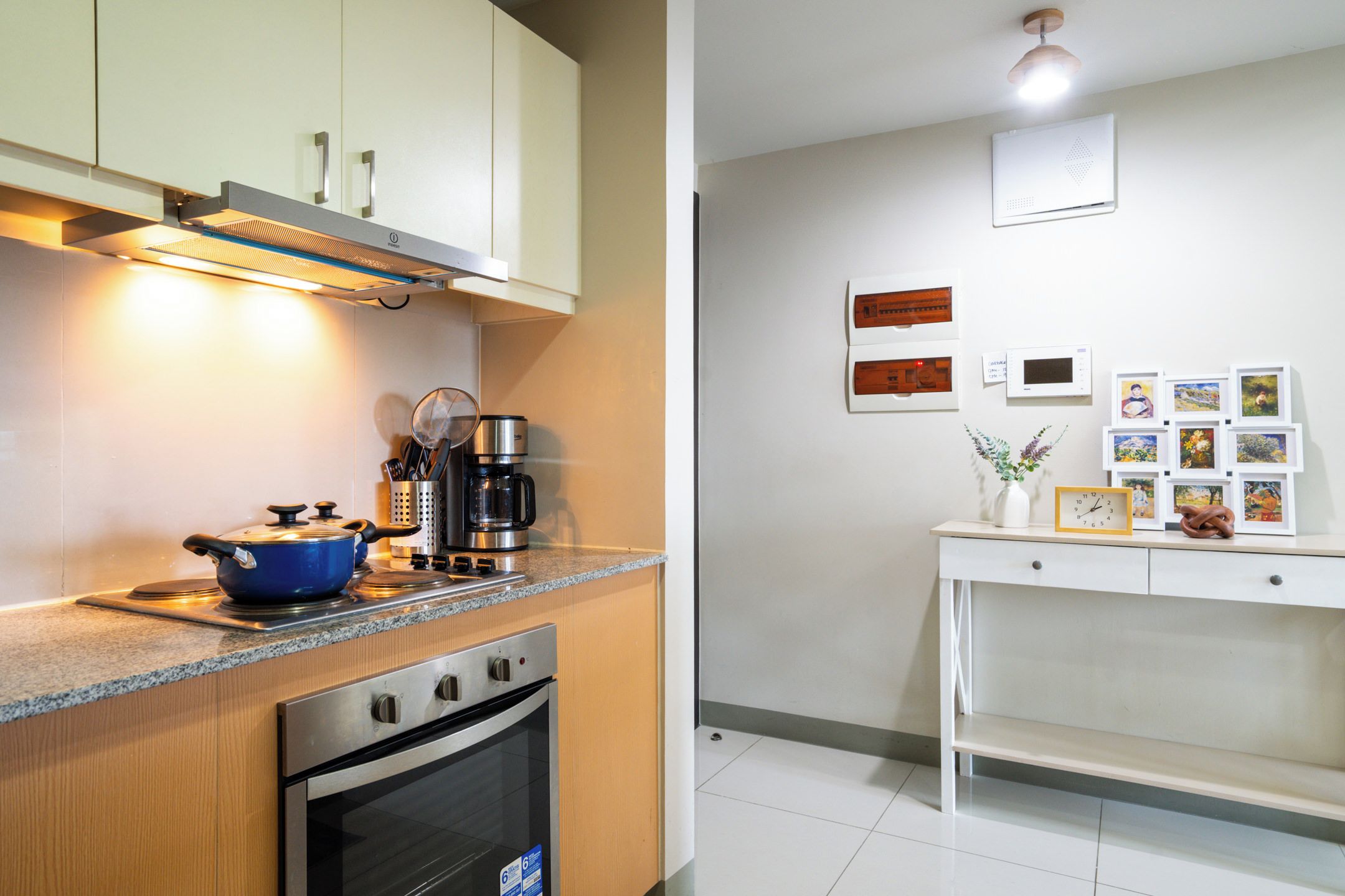 A modern kitchen with a stove, coffee maker, and a dining area with a table and framed pictures.