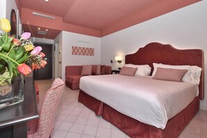 A hotel room with a large bed, a sofa, a desk, and a vase of flowers.