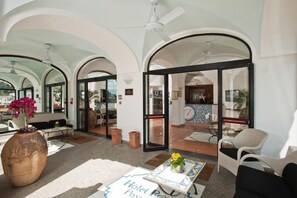 A hotel lobby with arched ceilings, a reception desk, seating area, and a view through the glass doors.
