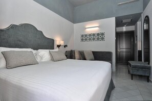 A modern hotel room with a large bed, a bedside table, a wall-mounted lamp, and a door leading to a bathroom.