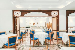 A dining area with round tables, blue chairs, and a kitchen in the background.
