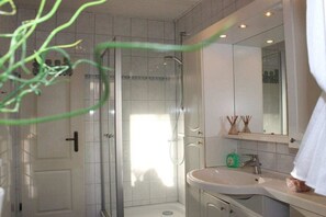 Een badkamer met een douche, wastafel en spiegel.