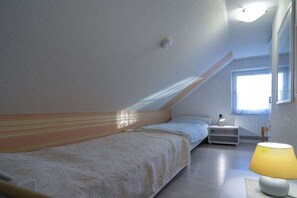 Een slaapkamer met een schuine kap, een bed, een nachtkastje met een lamp en een raam.