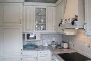 A kitchen with white cabinetry, a microwave, a coffee maker, and a toaster. - Holiday home with 2 bedrooms (Dornumersiel)