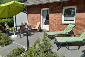 A patio area with outdoor furniture, including a table, chairs, and lounge chairs, and a green umbrella providing shade. - Holiday home with 2 bedrooms (Dornumersiel)