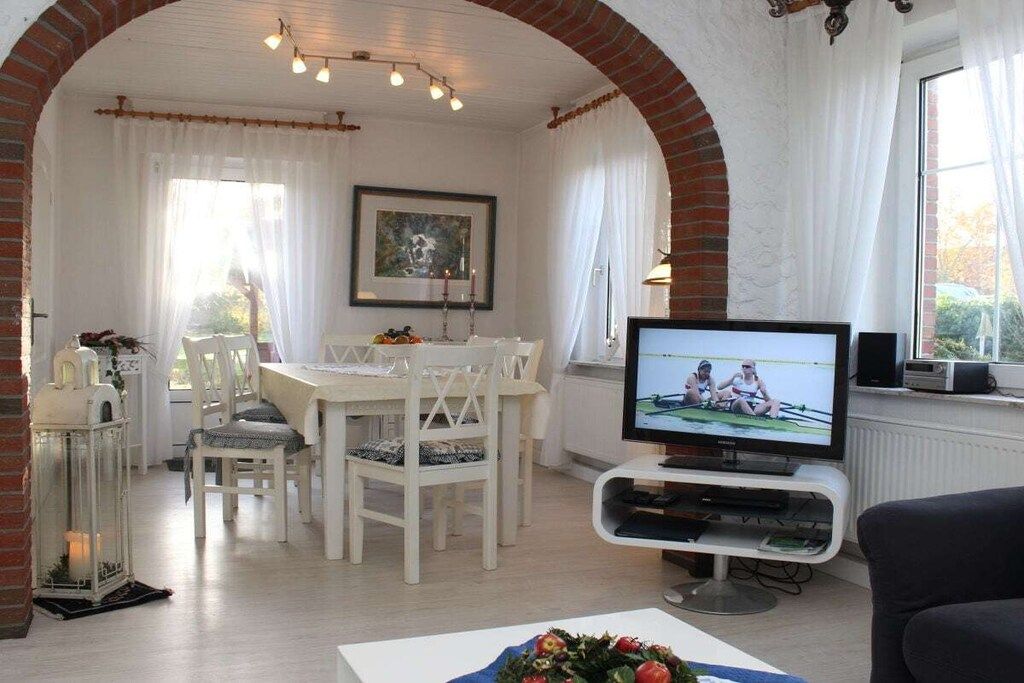 Una sala de estar con televisor, un comedor con mesa y sillas, y un arco de ladrillo.