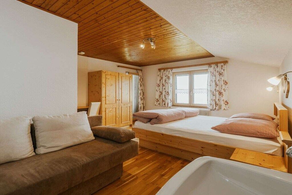 Een slaapkamer met een houten plafond, een bed met kussens, een houten kledingkast en een raam met gordijnen.