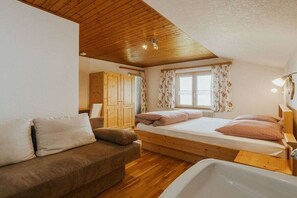 Een slaapkamer met een houten plafond, een bed met kussens, een houten kledingkast en een raam met gordijnen.