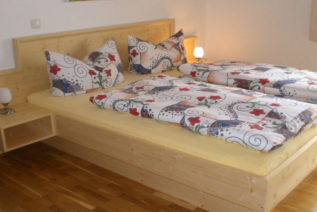 Un lit double avec une literie à motifs floraux, une table de chevet avec une lampe et une tête de lit en bois.
