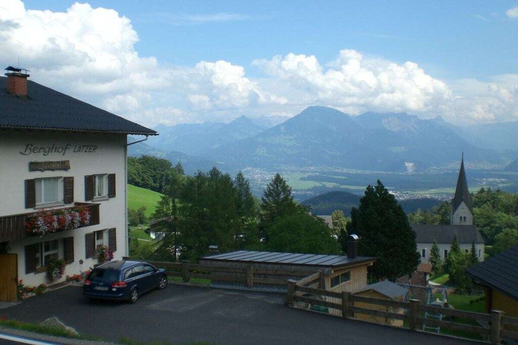 Ein Gebäude namens 'Berghof Latzier' mit Blick auf Berge und eine Kirche im Hintergrund.