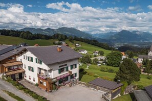 A two-story building with a balcony, surrounded by a well-maintained lawn and a mountainous backdrop. - Holiday apartment with 2 bedrooms (Gurtis)