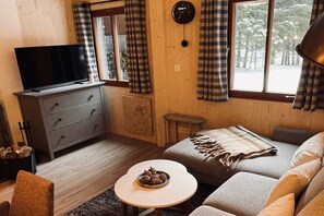 A cozy room with a television on a dresser, a sofa, a small table with a bowl, and a window with curtains. - Ski lodge in Ebene Reichenau with sauna (Ebene Reichenau)