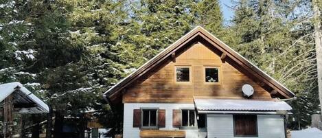 A wooden cabin with a gabled roof, surrounded by snow-covered trees.