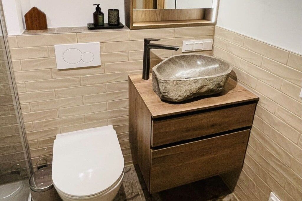 A bathroom with a stone sink, wooden vanity, and a toilet.